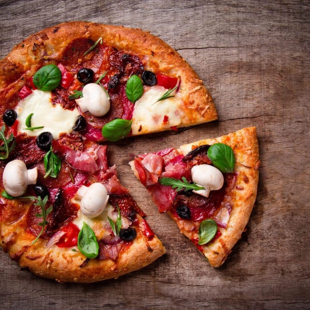 A pizza cut in half on top of a wooden table.